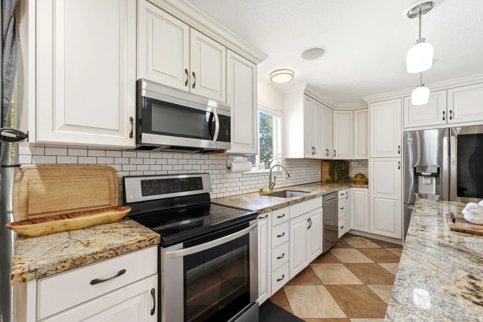 White shaker-style cabinetry, stainless steel appliances, granite countertops, white subway tile backsplash, and patterned tile flooring