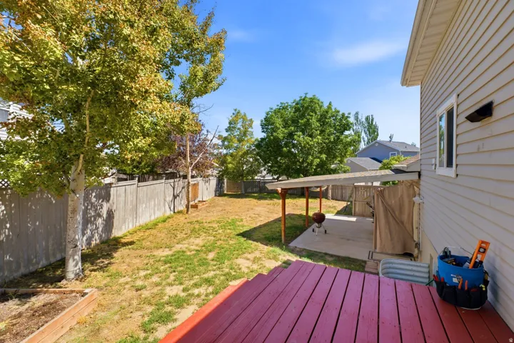 Expansive backyard with a wood privacy fence, mature trees, a red wood-finish deck, and a covered concrete patio