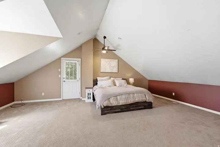 Carpeted room with vaulted ceilings, a ceiling fan, and a white paneled door with integrated blinds