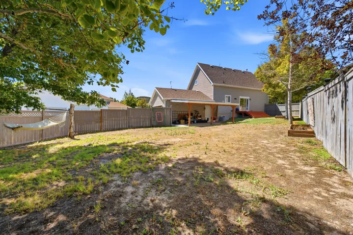 Expansive backyard featuring a covered patio, wood fencing, and mature trees