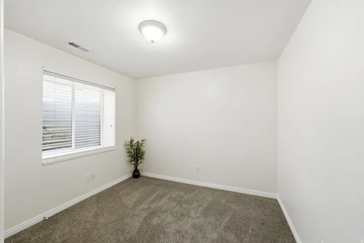 Bright secondary bedroom featuring neutral wall finishes, carpet flooring, and a large window with horizontal blinds allowing natural light