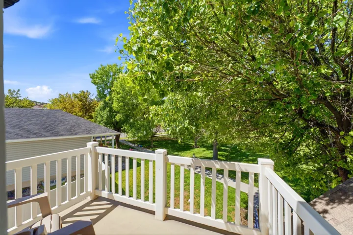 Private balcony off second floor primary bedroom with white railing and concrete flooring overlooking green landscaping and mature trees