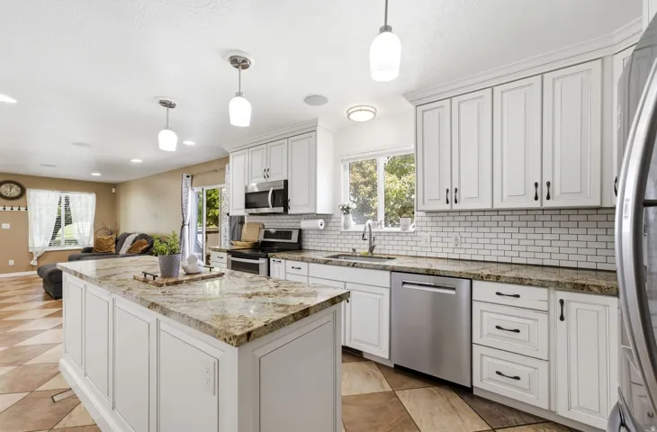Kitchen featuring white cabinetry, granite countertops, subway tile backsplash, stainless steel appliances, and a central island