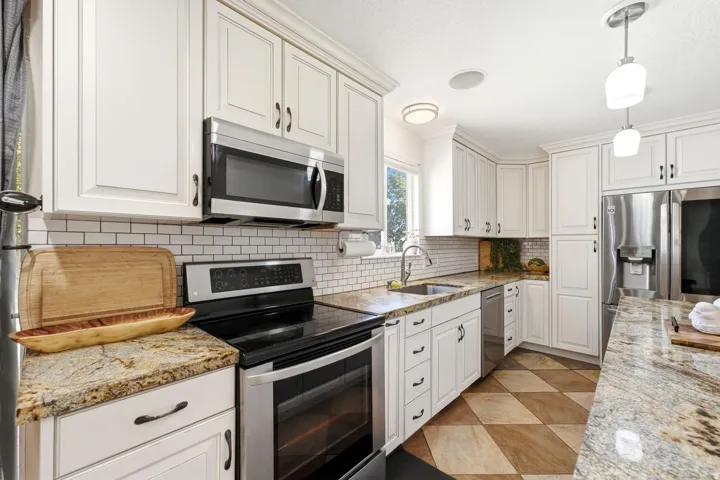 White shaker-style cabinetry, stainless steel appliances, granite countertops, white subway tile backsplash, and patterned tile flooring