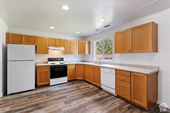 Kitchen featuring wood-finish cabinetry, light-toned countertops, wood-finish flooring, white appliances, and a window