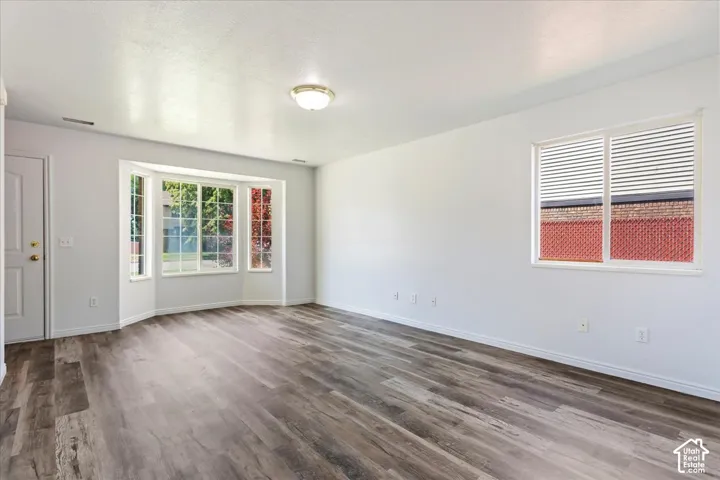Spacious room featuring wood-finish flooring, a prominent bay window, and white walls