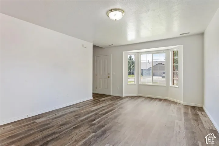 Wood-finish flooring, bay window, white walls, flush mount ceiling light, and a paneled entry door
