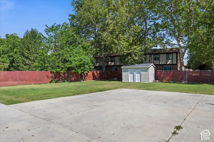 Expansive concrete patio with a detached storage shed, lush green lawn, and mature trees