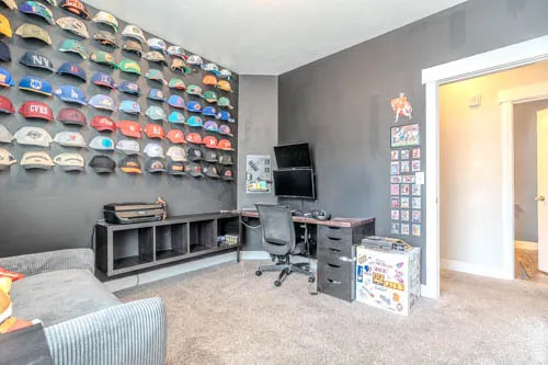 Dedicated hobby room featuring wall-mounted display shelving with extensive storage capacity, carpeted flooring, built-in desk workspace with task lighting, and gray accent walls