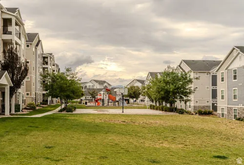 Expansive green space featuring a manicured lawn, paved walkways, mature trees, and a visible playground structure