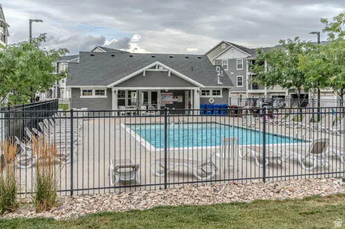 Community swimming pool with a surrounding concrete deck, black metal fencing, and adjacent clubhouse building