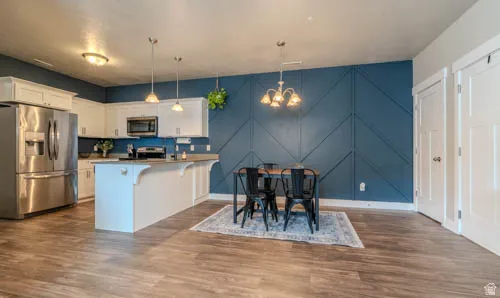 Open-concept living space with wood-finish flooring, white cabinetry, stainless steel appliances, and a kitchen island with pendant lighting