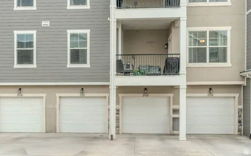 Exterior featuring multiple garage doors, a second-story balcony with iron railings, and upper-level windows