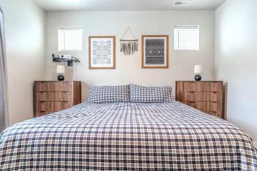 Primary bedroom featuring wood-finish nightstands with integrated shelving, blue and white plaid bedding, and framed wall art