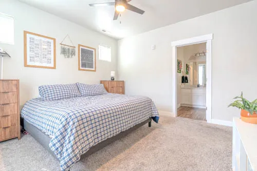 Spacious primary bedroom with soft carpeting, ceiling fan with integrated lighting, and direct access to an ensuite bathroom