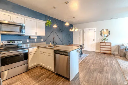 Modern kitchen featuring stainless steel appliances, white cabinetry, a kitchen island with sink, and wood-finish flooring