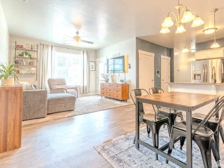 Open-concept living and dining area featuring wood-finish flooring throughout, a dining table with seating for four, and abundant natural light from large windows