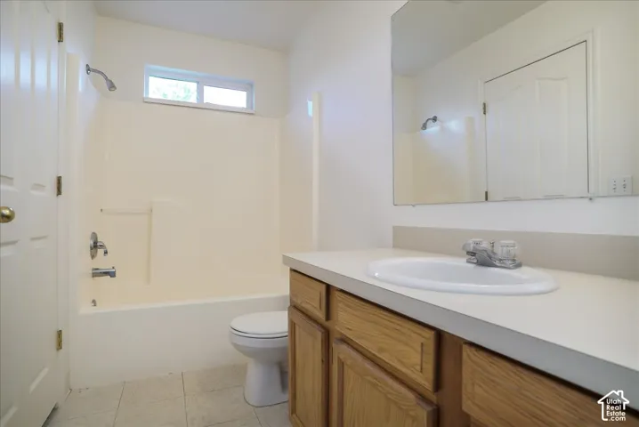 Bathroom with a built-in tub and shower combination, a window above the shower, a toilet, a vanity with a laminate countertop, and a wall-mounted mirror