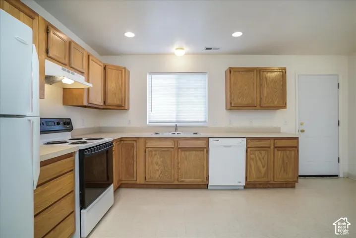 Kitchen featuring wood cabinetry, white appliances, a built-in dishwasher, and a window with blinds