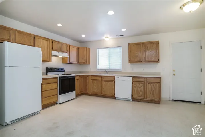 Kitchen featuring wood cabinetry, white appliances, recessed lighting, and a double-basin sink