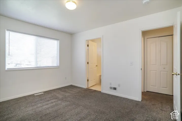 Neutral wall paint, gray carpeting, window with blinds, overhead flush mount light, and bi-fold closet doors