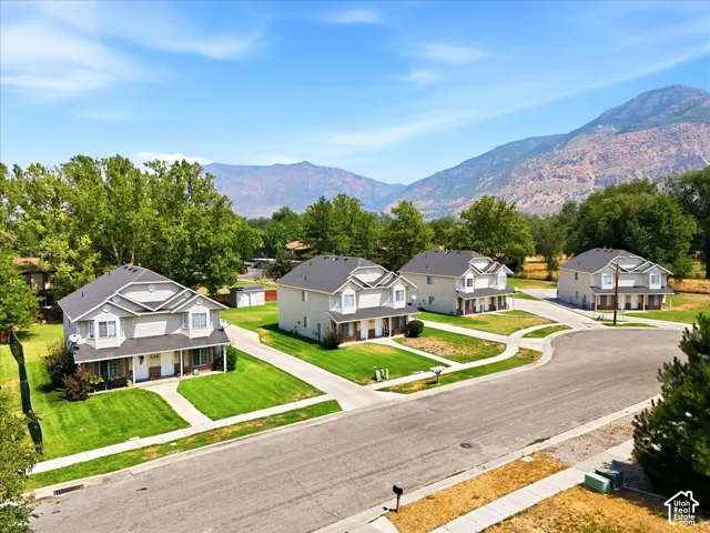 Residential street with multiple two-story homes, individual driveways, green lawns, and a mountain backdrop