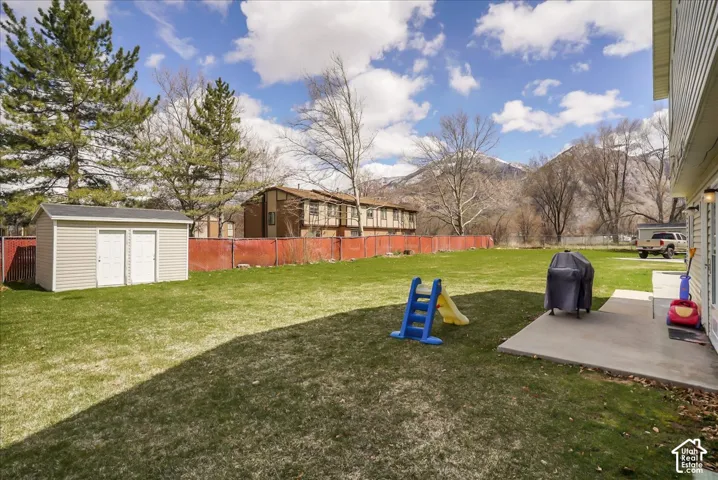 Expansive green lawn, concrete patio, mountain backdrop, and a detached storage shed with double doors