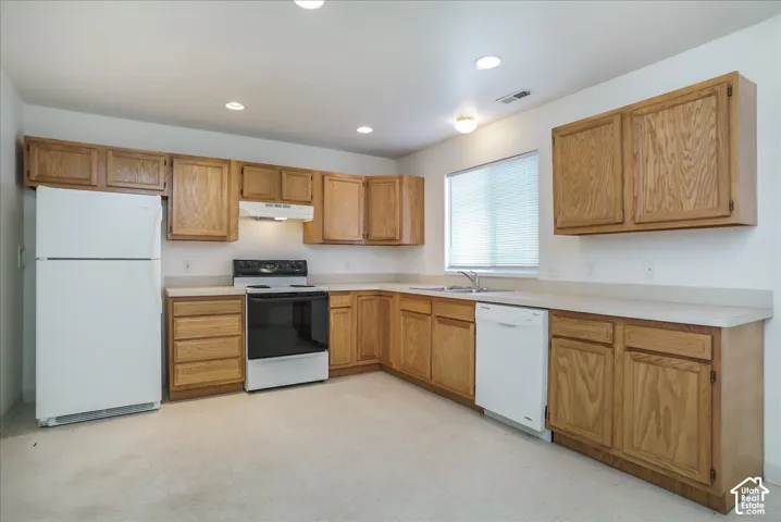 L-shaped kitchen featuring wood-finish cabinetry, solid surface countertops, white appliances, and a double basin sink