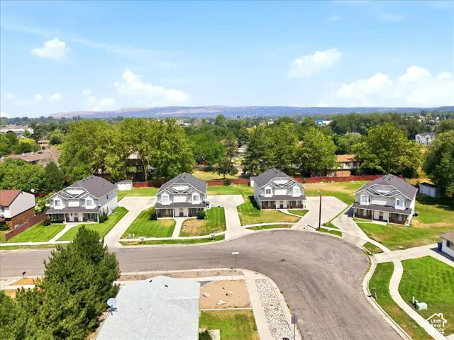 Residential street with multiple properties featuring light-colored exteriors, dark roofs, and green lawns