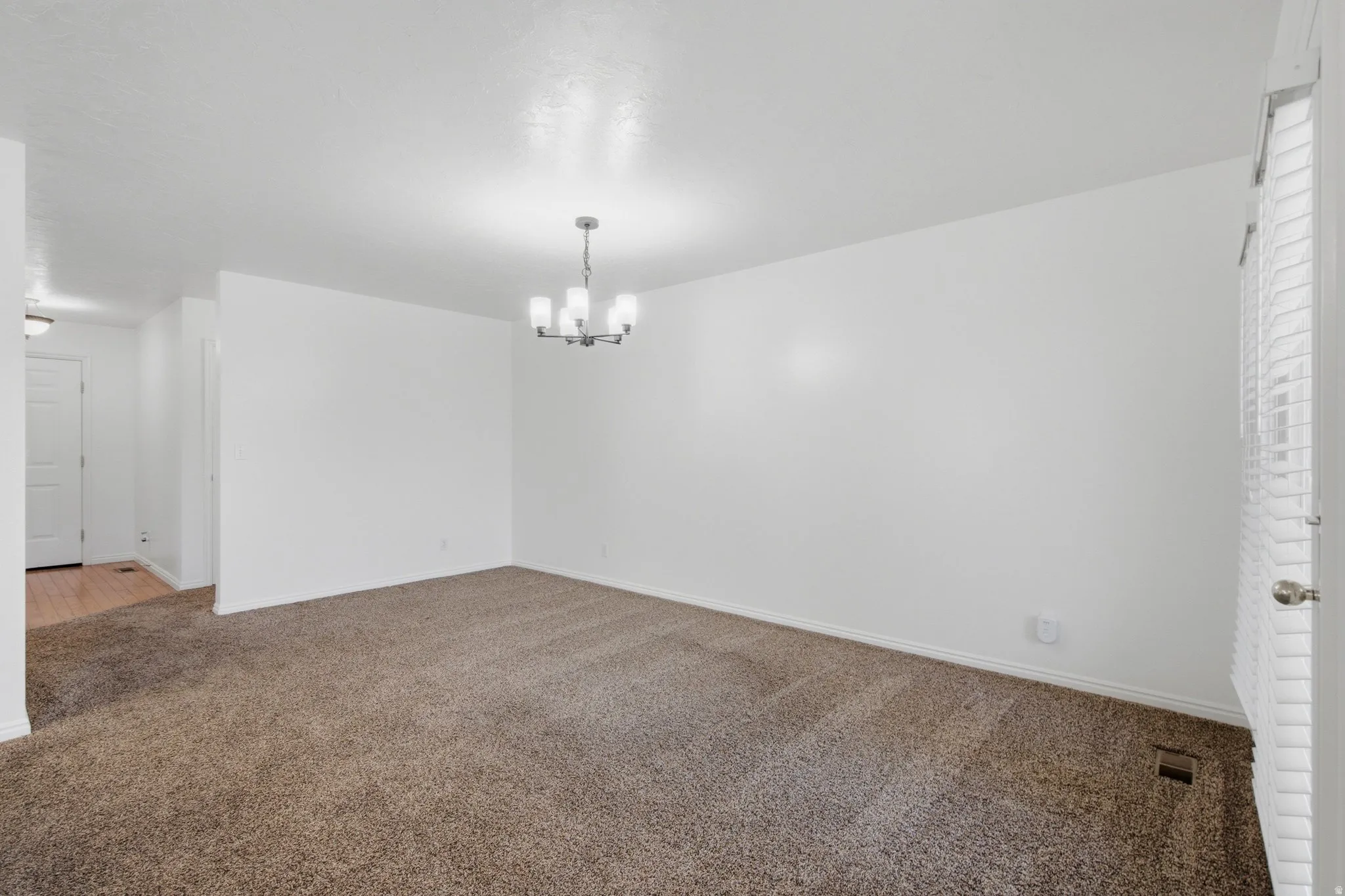 Spacious room with plush carpet flooring, a contemporary chandelier, and white wall finishes