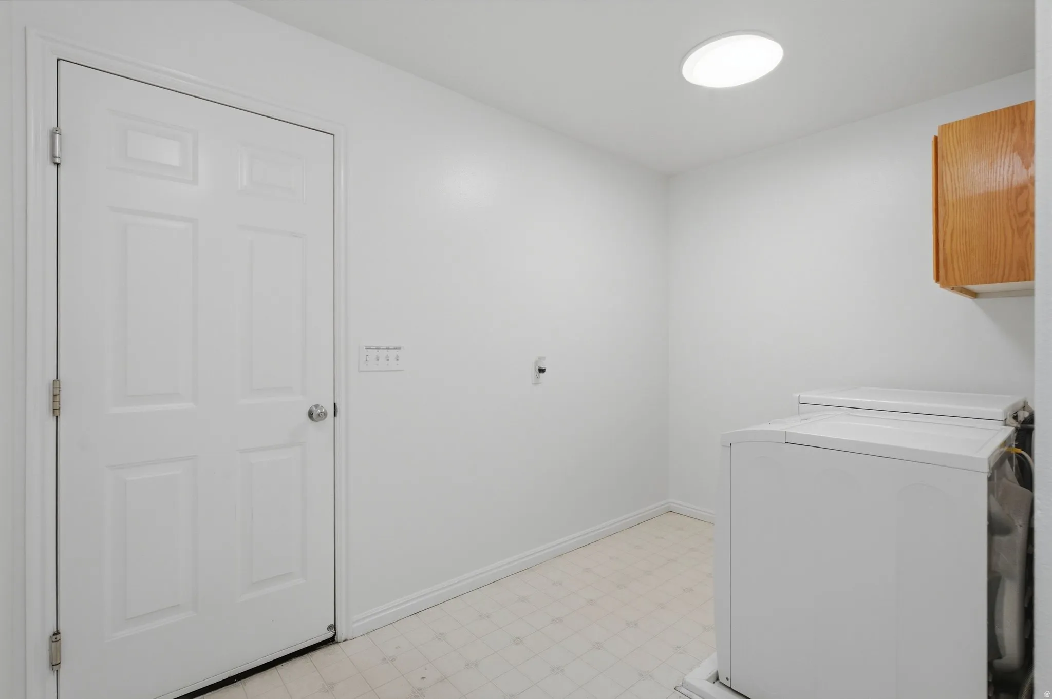 Laundry area featuring a skylight, light wood-finish cabinetry, and panel doors