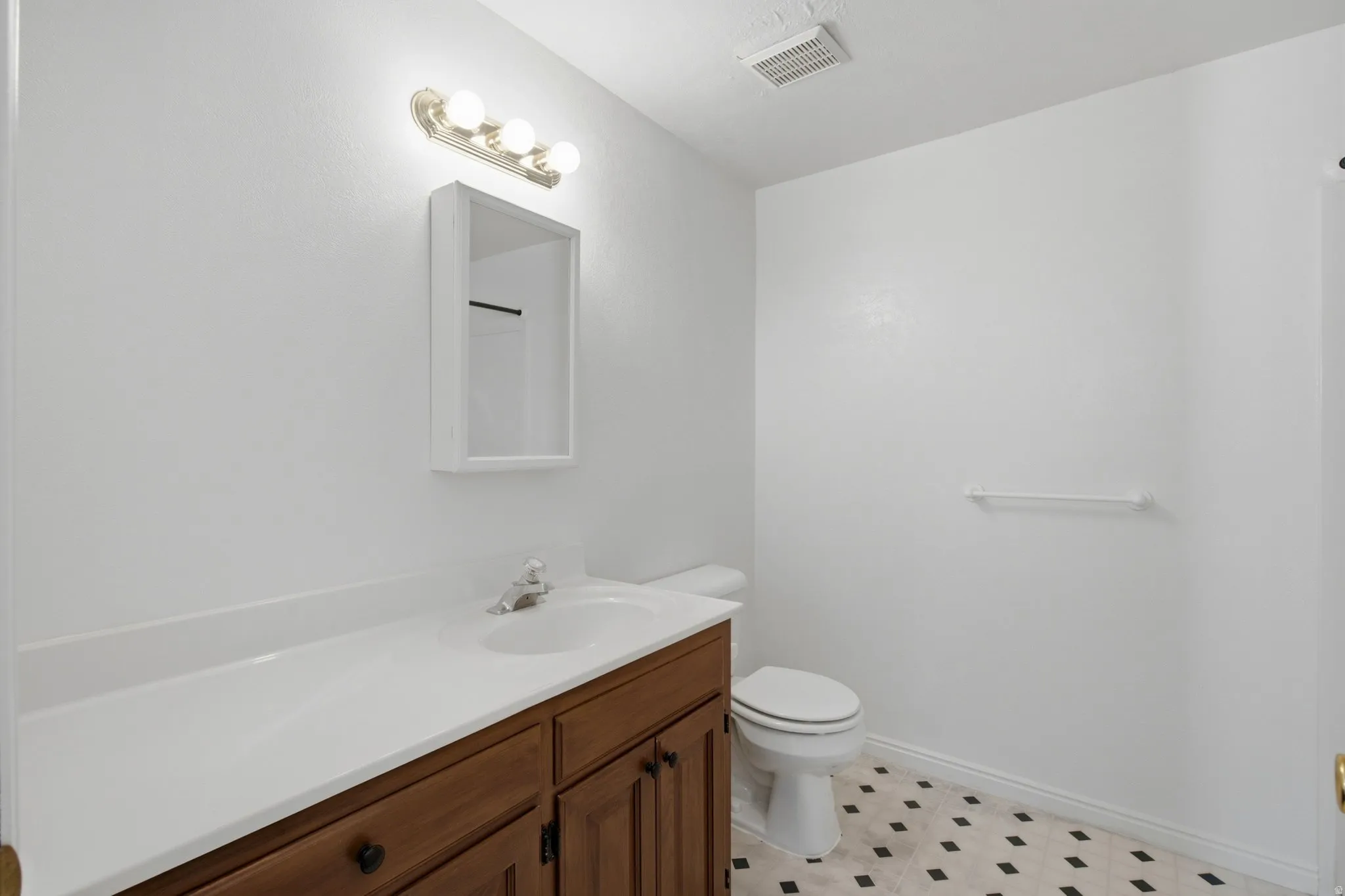 Vanity with integrated sink and chrome faucet, medicine cabinet, three-bulb vanity light, toilet, and patterned floor tile