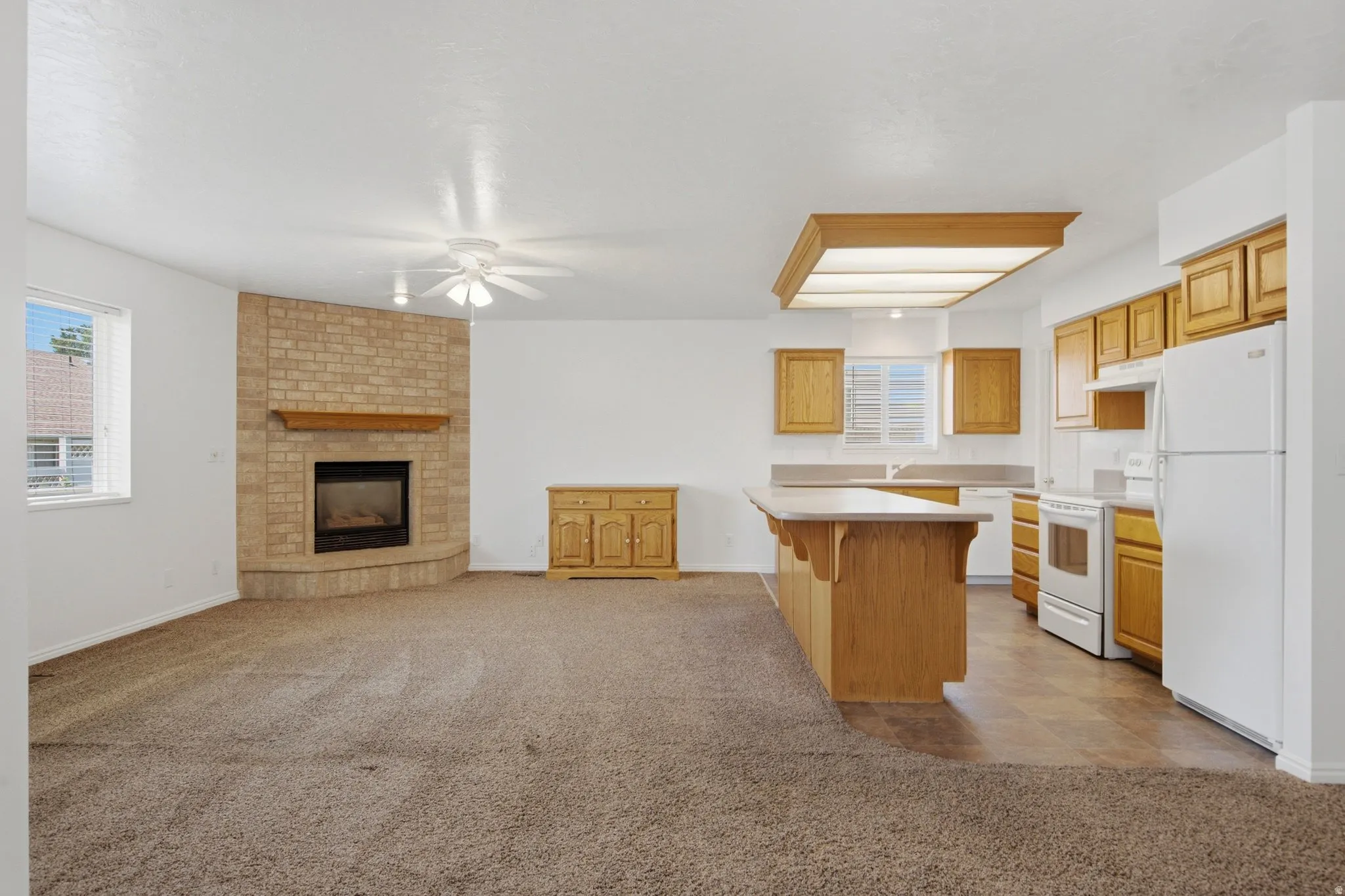 Open-concept living area with a corner brick fireplace and a ceiling fan