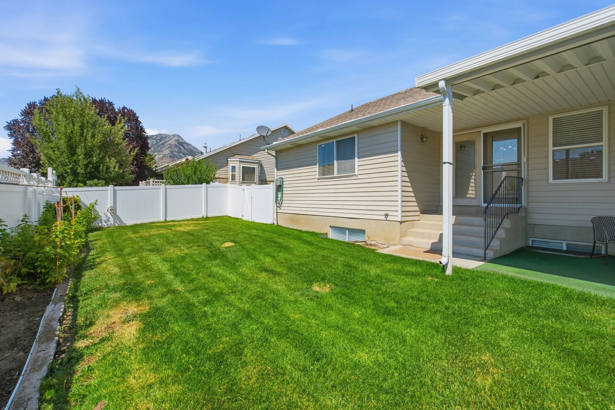 Expansive backyard featuring a manicured lawn, white privacy fence, and a covered patio with concrete steps