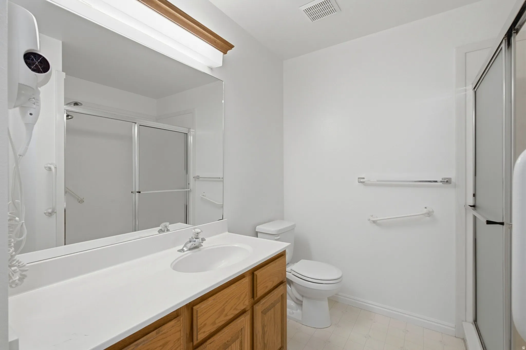 Bathroom featuring a wood-finish vanity, white countertop, integrated sink, and a shower with sliding glass doors