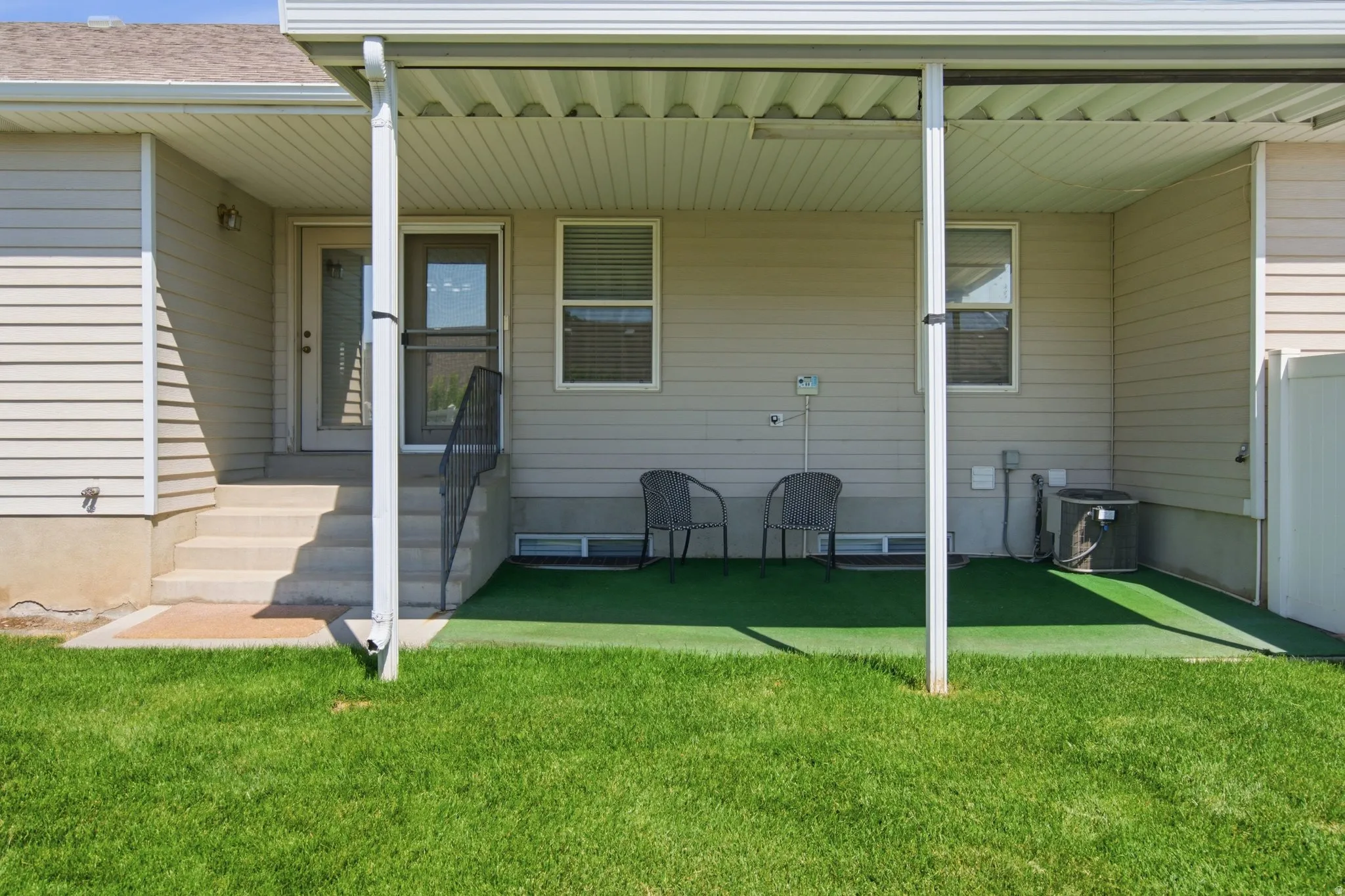 Covered patio with an artificial turf surface and a white vinyl fence