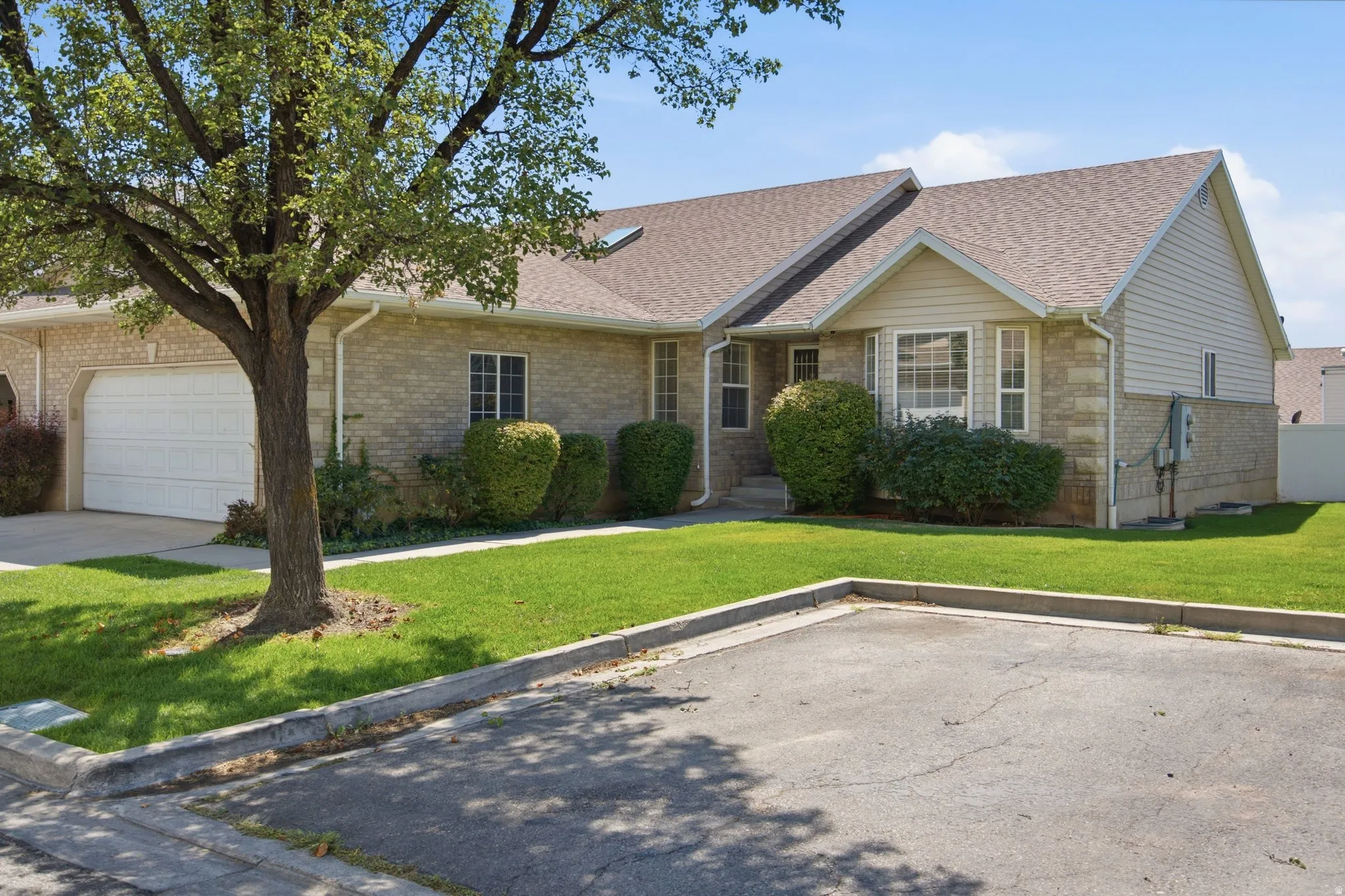 Brick veneer exterior with siding accents, gabled roofline, front-facing garage, and established landscaping