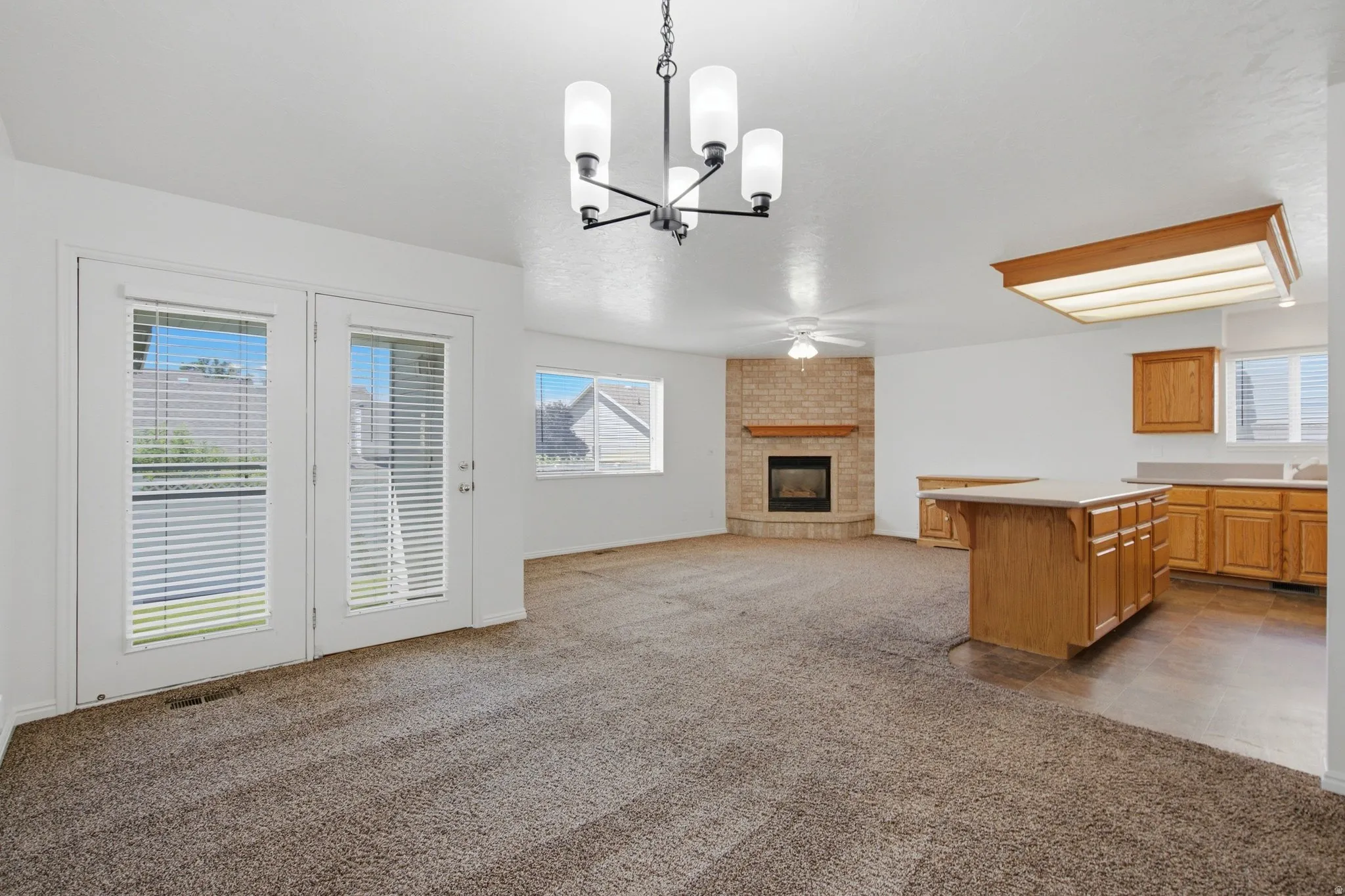 Dual French doors, corner fireplace with brick surround, kitchen with wood cabinetry, kitchen island, and overhead fluorescent lighting