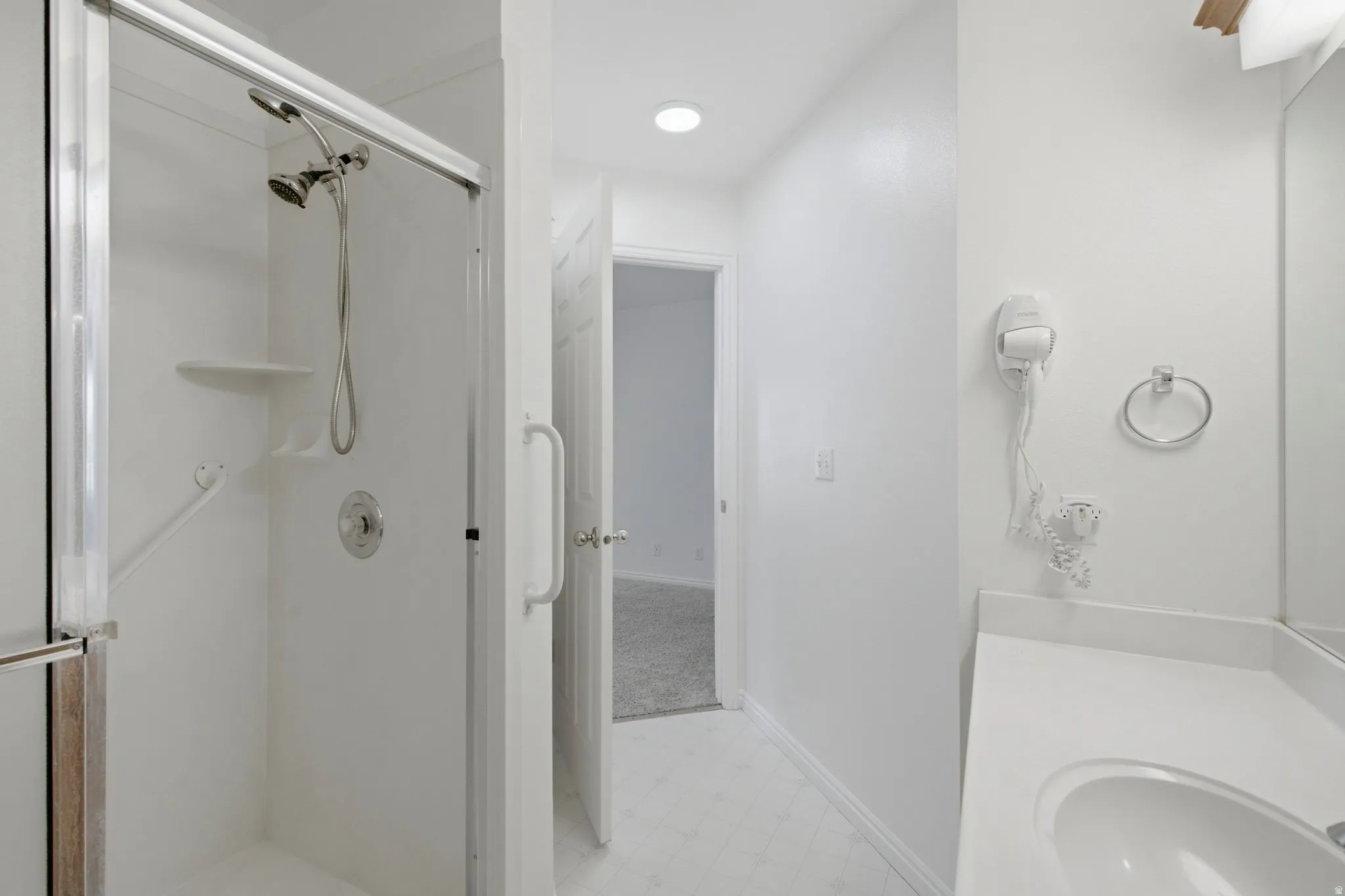 Walk-in shower with grab bars and built-in shelving, white vanity with integrated sink, and wall-mounted mirror