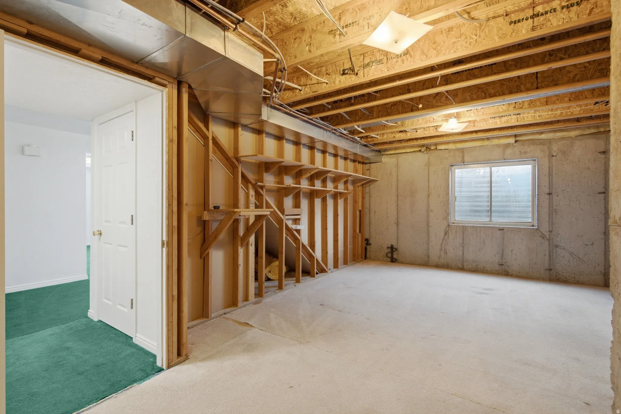 Unfinished space with exposed ceiling joists, concrete walls, and a visible window