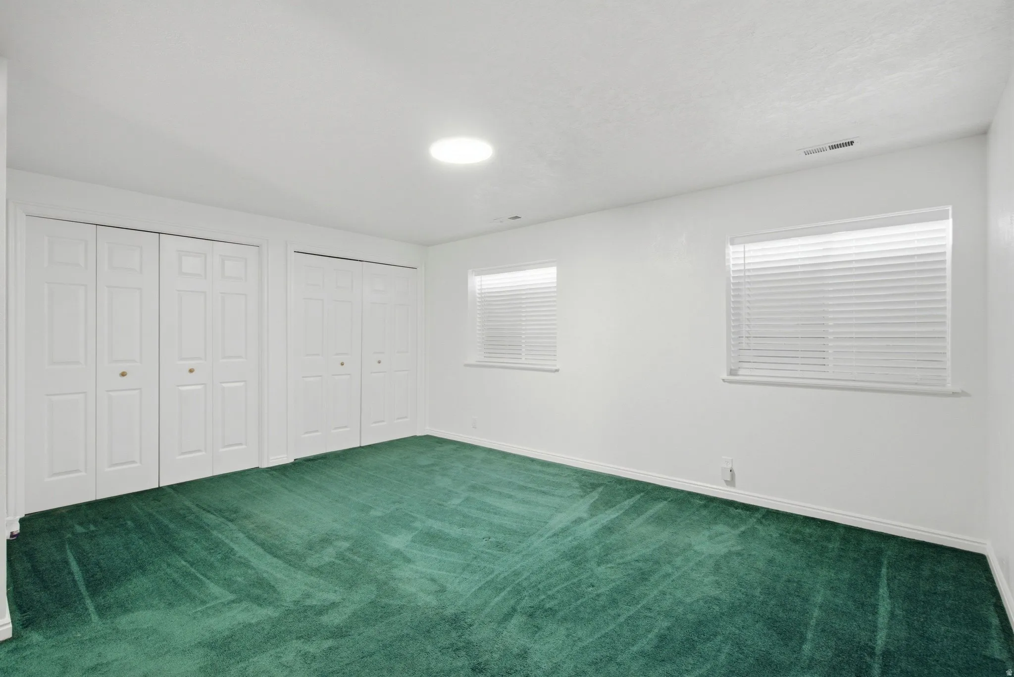 Dual white bi-fold closets, two separate windows with blinds, and recessed lighting