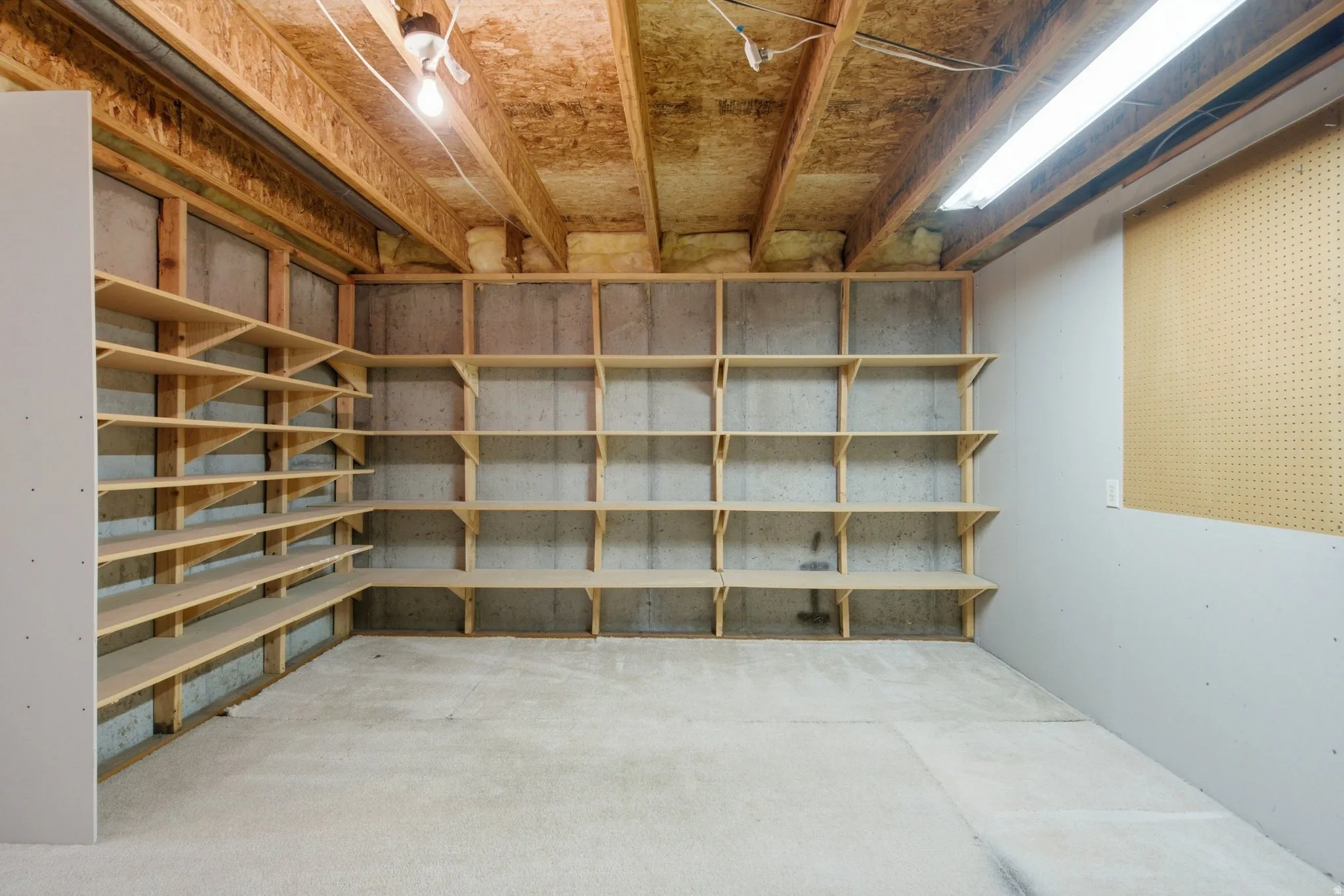 Unfinished basement storage room featuring exposed wood-beam ceiling, concrete flooring, and built-in wooden shelving units along two walls