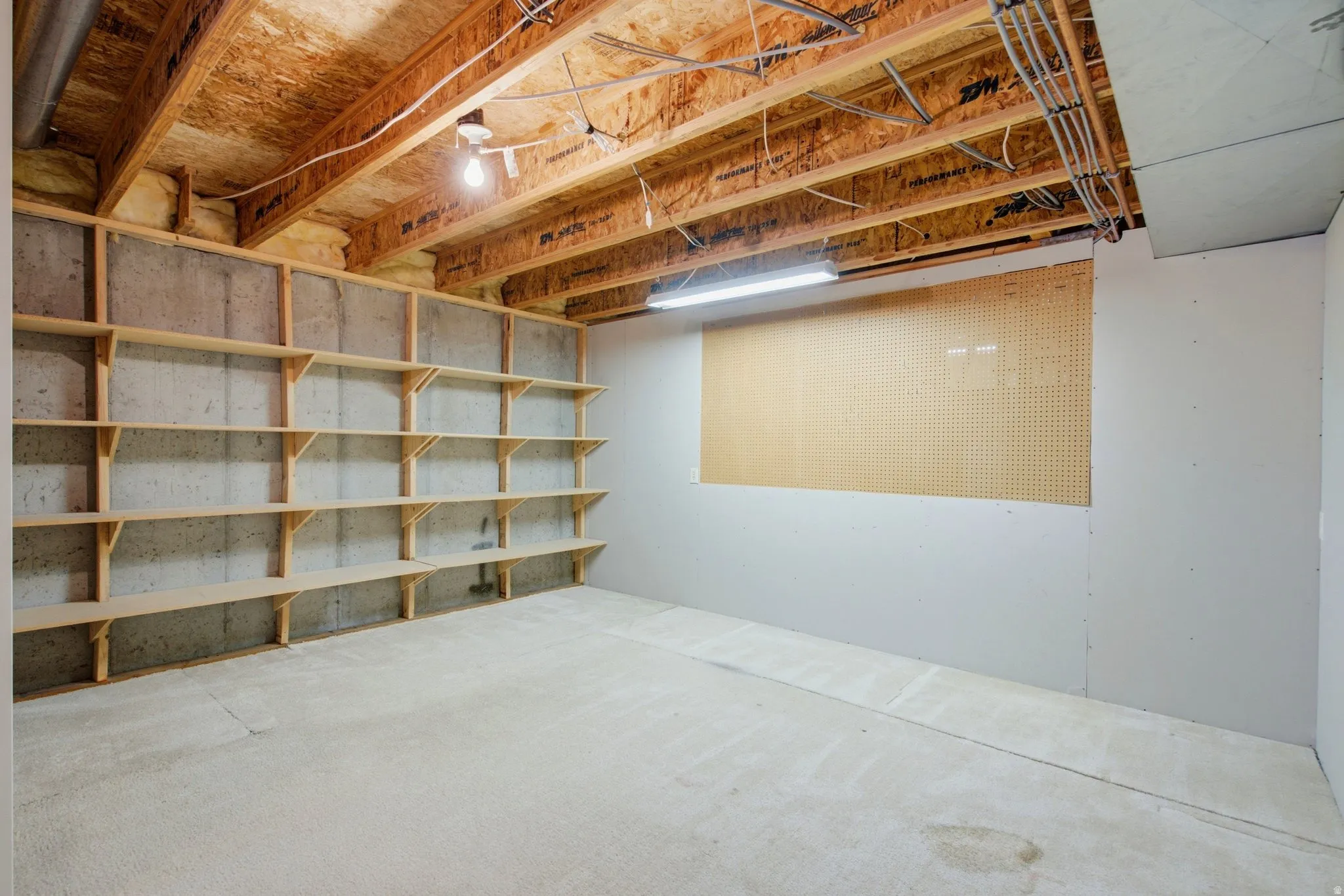 Unfinished basement with exposed ceiling joists, concrete flooring, extensive built-in shelving, and a large pegboard wall