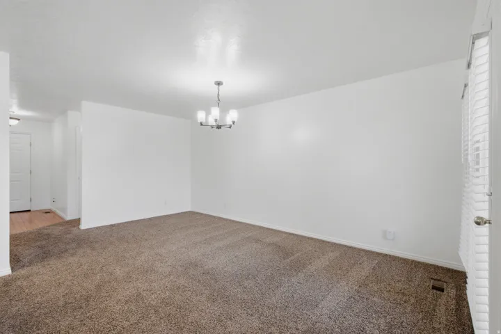 Spacious room with plush carpet flooring, a contemporary chandelier, and white wall finishes