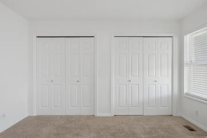 Dual bi-fold closet doors, neutral wall paint, window with blinds, and carpeting