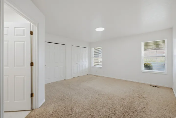 Neutral carpet flooring, white walls, two bi-fold closet doors, and two windows with horizontal blinds