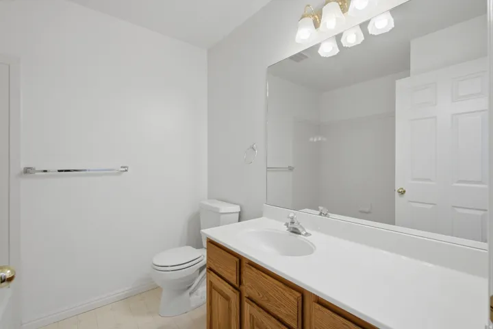 Vanity with wood-finish cabinetry and integrated sink, large wall-mounted mirror, overhead vanity lighting, and white toilet