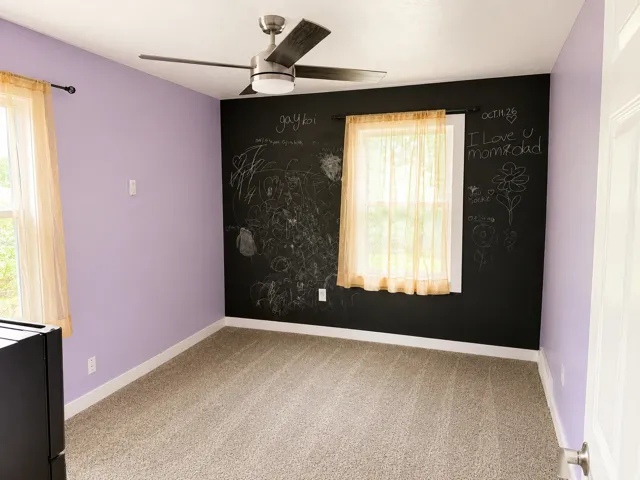Carpeted flooring, a ceiling fan with integrated lighting, window with trim, and a feature wall