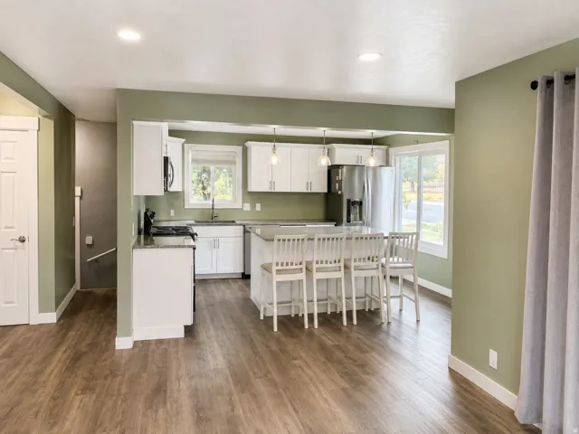 Open-concept kitchen featuring white cabinetry, stainless steel appliances, a center island with seating, and wood-finish flooring