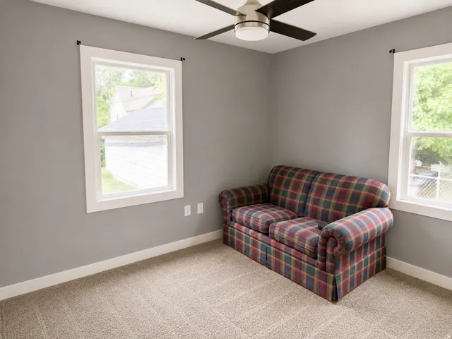 Neutral wall paint, carpeting, ceiling fan with integrated lighting, and two bright windows with white trim